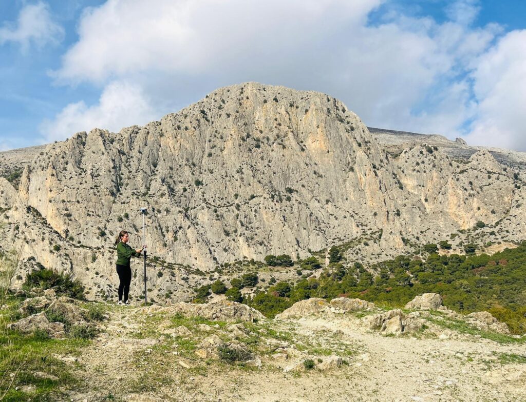 Topógrafa realizando medición geodésica en un entorno montañoso con equipo GPS de precisión en Málaga